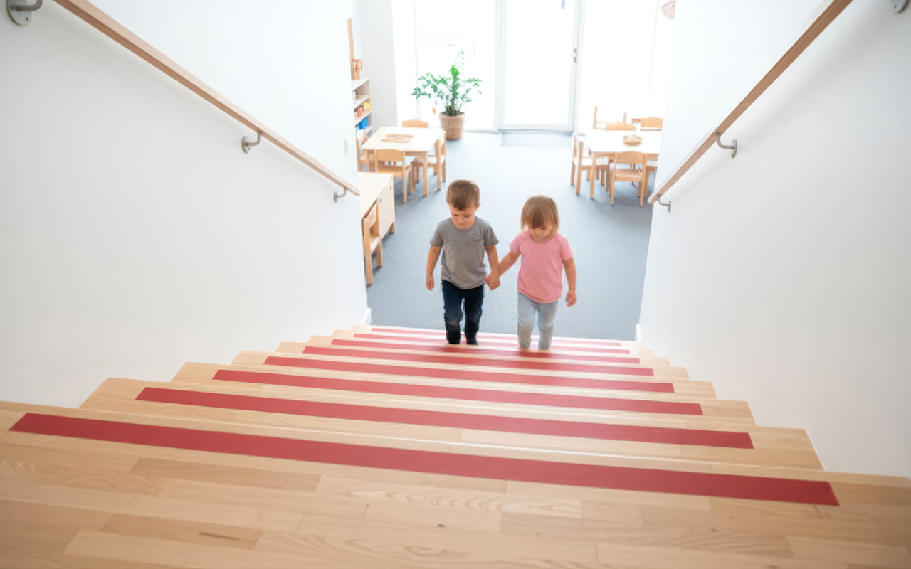 Red anti-slip strips on the treads of a wooden staircase, with two children walking up.