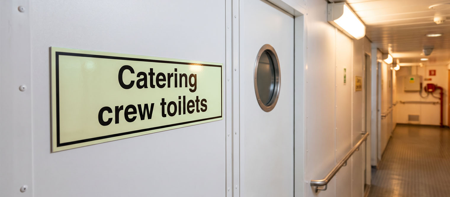 Toilet or facility signage in a ship's accommodation corridor.