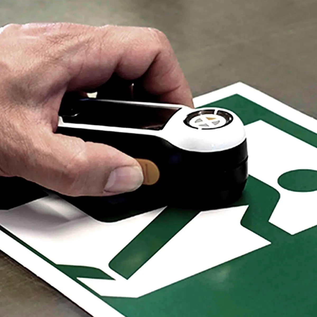 A handheld colour meter measuring the green of an emergency exit sign.